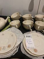 Photo showing a group of eight teacups stacked and arranged behind several saucers with a dandelion design.
