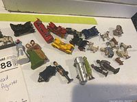 Set of 26 varied weathered lead figures including people, animals, and vehicles arranged on a white surface.