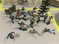 Photo of 20 hand-painted lead soldier figurines in blue Union and grey Confederate uniforms posed with accessories including a green tree and stone wall fence.