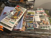 Overview of scrapbooking supplies including sticker sheets, packs, paper cutter and craft paper on a table.