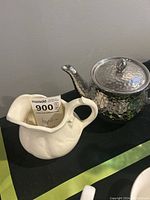 Image showing hammered silver teapot and white ceramic creamer together on a black surface