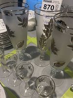 Photo showing three tall frosted beer glasses with silver leaf design and four small clear shot glasses, to illustrate the entire set and design details.