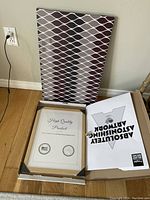 MCM design pattern canvas with geometric repeating pattern standing vertically against wall with brown wooden floor, next to a framed artwork in box.