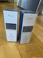 Two unopened boxes of TOTCLEAR Dark Spot Corrector on a wooden floor, showing front and side of boxes.