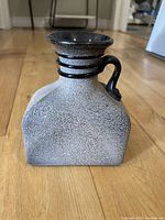 Side view showing speckled gray textured body, black handle and circular bands around the neck.