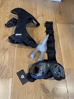 Photo shows the black mesh dog harness, gray plastic tail leash hook, and black dog goggles with tint from the front view.