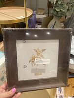 Photo of new 7-inch square brown wood picture frame still shrink-wrapped in plastic on wooden table