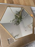 Gold hexagon mirror resting on cardboard box showing reflective surface, gold frame, and hanging chain.