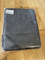 Photo showing front view of grey cloth iPad carrying case sealed in plastic packaging on wooden floor.