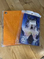 Two unopened tablet cases: one orange with embossed floral pattern, one blue with wolf and moon graphic