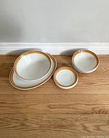 Johnson Brothers Ironstone oval serving platters, bowls, and saucers with golden orange rim arranged on a floor.