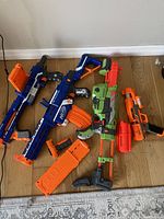 Lot of four Nerf blaster toys displayed on the floor showing various sizes and colors including blue, green, and orange.
