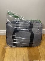 Grey insulated cooler bag wrapped in plastic, showing overall shape and carry handles.