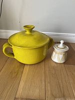 Photo showing both vintage ceramic pots on wooden floor, the larger yellow pot with lid and handles and smaller cream and brown pot with lid.