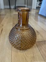 Front and side views of a small amber glass vase with a bulbous textured diamond-pattern round body and narrow, flared neck.