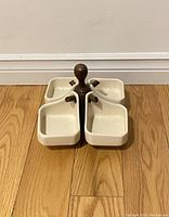 Full view of the vintage ceramic serving dish with four square sections and a central dark wooden handle against a light wall and wood floor background.