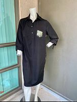 Front view of the black dress showing long sleeves rolled up, sequin chest pocket, and side pockets on a mannequin.