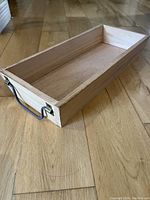 Angled side view of rectangular wood tray showing one metal handle and overall natural wood finish.