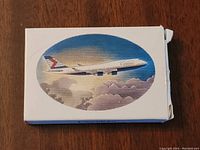 Two images of Air Canada playing card deck boxes on wooden surface showing front with airplane illustration.