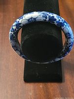 Blue Willow ceramic bangle displayed on black stand showing pattern and condition.