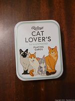 Front of metal tin showing colorful illustrations of four different cats and the brand name Ridley's with the title 'Cat Lover's 54 Illustrated Playing Cards'