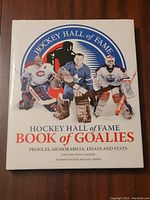 Front cover of the hardcover book titled 'Hockey Hall of Fame Book of Goalies' featuring color images of three famous hockey goalies in different uniforms.