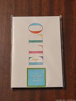 Front view of white notebook cover with 'HELLO' text and Kate Spade label affixed.