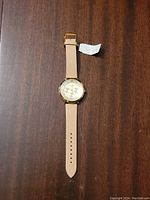 Full view of the Kate Spade ladies watch showing beige leatherette strap and gold-tone case with attached tag.