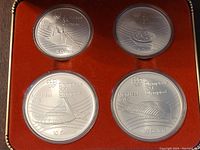Four silver Olympic coins in clear capsules displayed in red velvet interior of blue hinged box