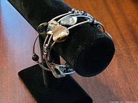 Set of three bracelets displayed on black stand, showing side view with shiny metallic beads.