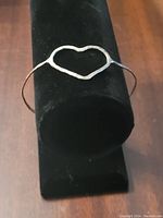 Silver metal heart shaped bangle displayed on a black stand showing front view of heart centerpiece and band