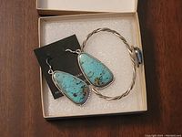 Pair of turquoise stone Navajo earrings and a silver twisted bracelet with turquoise stone in a box on a wooden table.