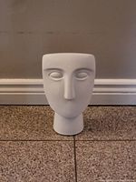 Front view of white ceramic face sculpture showing stylized facial features and smooth surface.