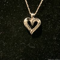 10K white gold heart-shaped pendant with diamonds displayed on black background.