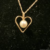 Close-up of the heart-shaped pendant with pearl centered on black background, showing design and materials clearly.