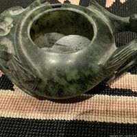 Close-up side view of dark green jade candle holder showing carved detail and coloration.