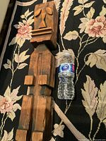 Photo showing the full length of the wooden tiki statue alongside a water bottle for size comparison, laid on a floral patterned rug.