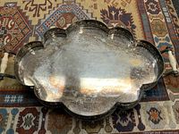 Top-down view showing scalloped border with pierced designs and reflective tray surface with signs of tarnish and wear.