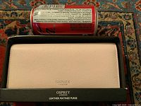 Light pink leather wallet/purse in original black box with Osprey London embossed on the wallet and box, placed beside a soda can for size reference.
