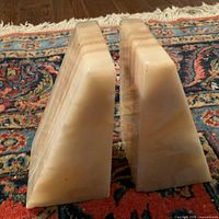 Pair of light beige marble bookends with a stepped trapezoidal design showing natural veining and minor nicks on a colorful rug background.
