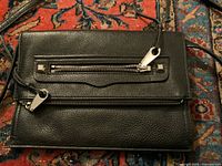 Front view of Rebecca Minkoff black leather purse showing front zipper pocket and adjustable strap.
