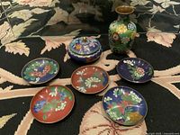 Photo of the entire cloisonné set including vase, lidded container, and six plates showing details and colors.