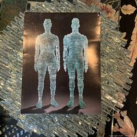 Front and side views of the glass sculpture represented in promotional photo, showing human-like forms made from stacked glass strips.