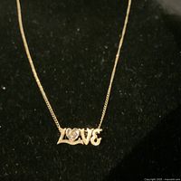 Photo of vintage 1970s 10K yellow gold LOVE pendant with heart-shaped stone on 10K gold chain displayed on black fabric background
