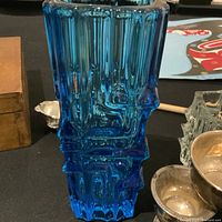 Photo capturing the side and top view of blue glass vase with visible geometric textured patterns on a table surrounded by other items.