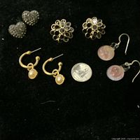Top-down view of four pairs of vintage costume earrings laid on black background with quarter for size reference.