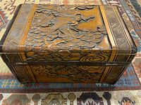 Front angle view of the carved wooden box showing the detailed figure on the lid and metal clasp on front.