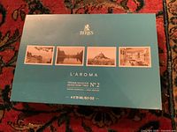 Image of unopened turquoise-blue Birks L’Aroma scented spray box with vintage photographic prints and product information.