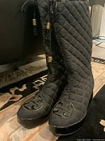 Photo showing both boots front view, highlighting the quilted fabric and Tory Burch logo on toe caps, lace details with brass ends (one missing)