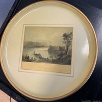 Full top view of vintage round transferware tray with beige rim and centered scenic print of a castle by a lake with boats and figures.